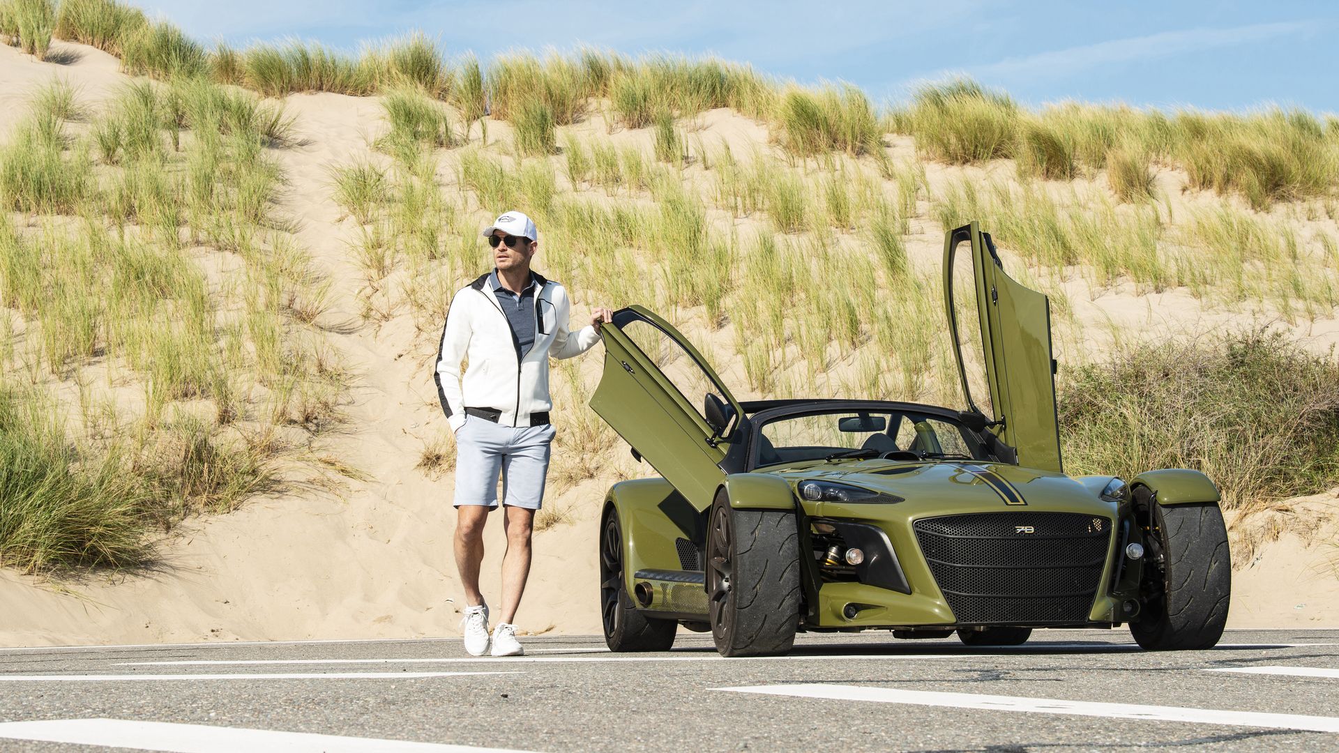 Man wearing white Donkervoort summer clothing next to a green D8 GTO-JD70
